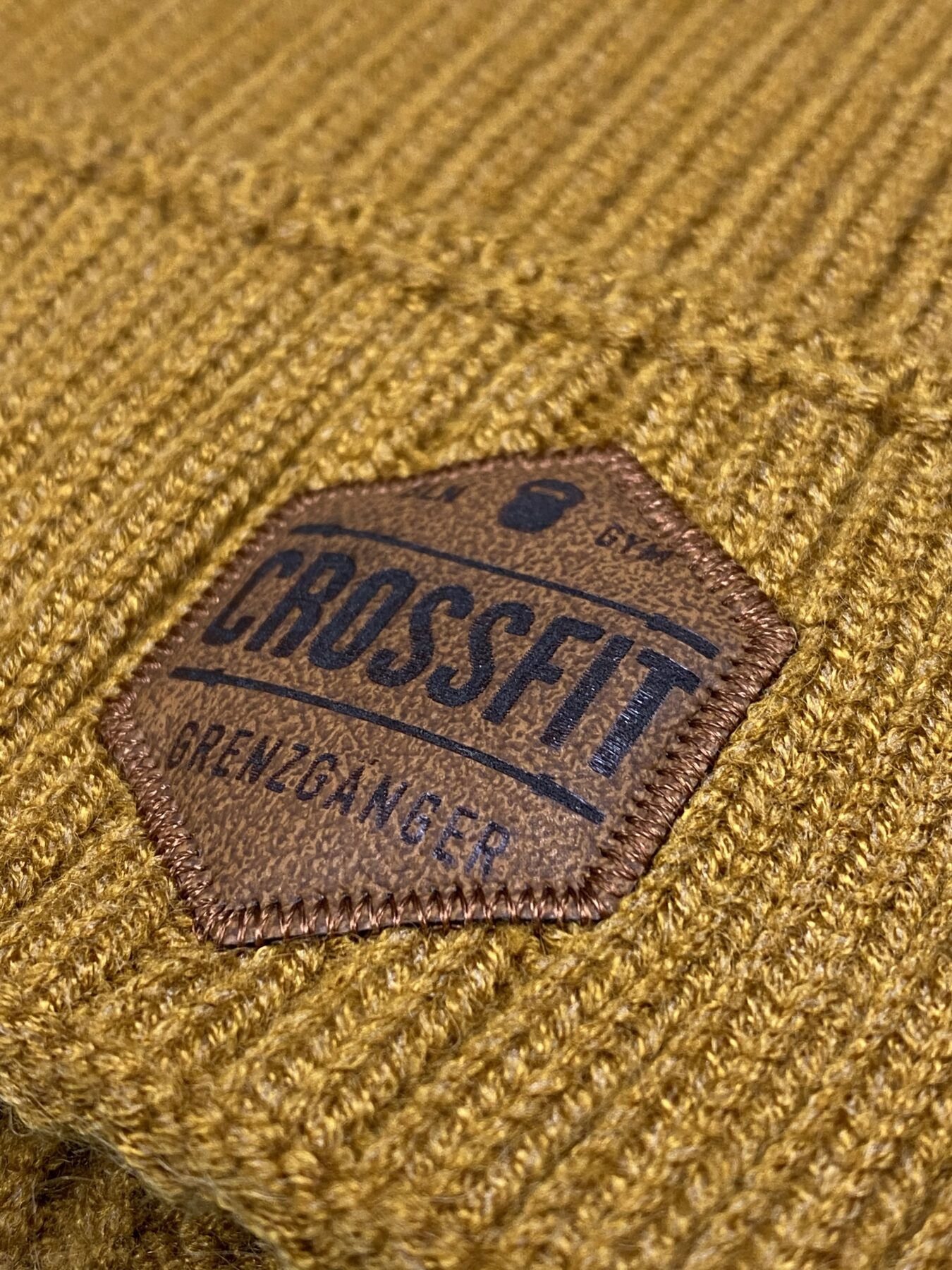 Lasergravierter Grenzgänger-Lederpatch auf senffarbener Strickmütze